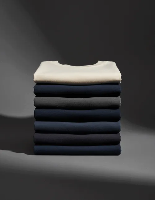 A stack of seven folded t-shirts in earth tones